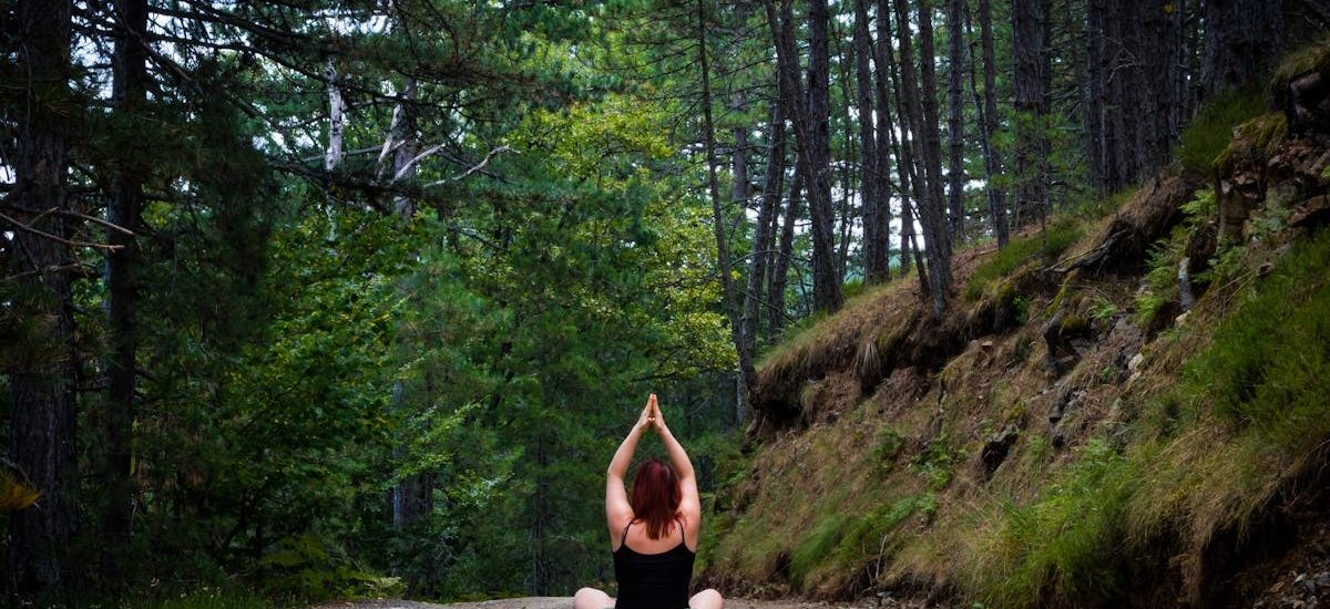 Woman practicing yoga in a tranquil forest setting, symbolizing peace and nature.
