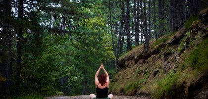 Woman practicing yoga in a tranquil forest setting, symbolizing peace and nature.