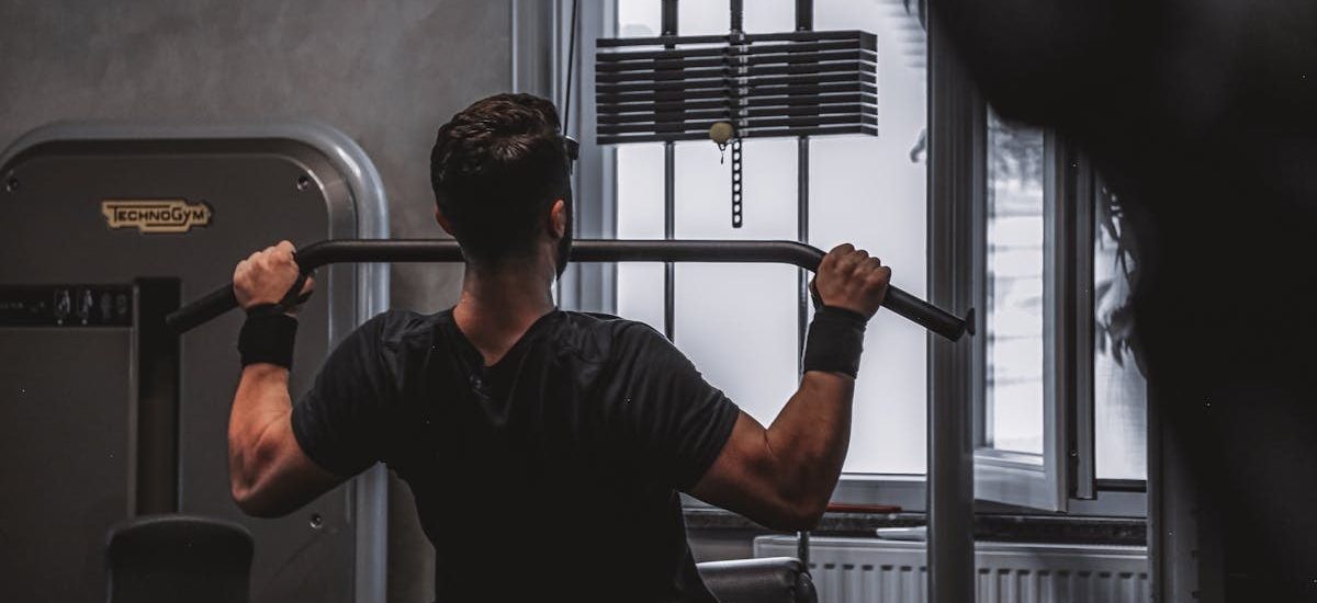 Back view of a man exercising with lat pulldown machine in the gym.