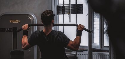 Back view of a man exercising with lat pulldown machine in the gym.